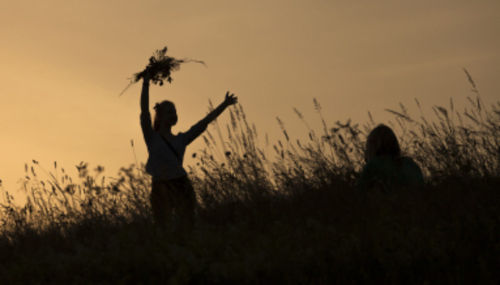 Silhouettes of happy girl picking flowers during midsummer solti