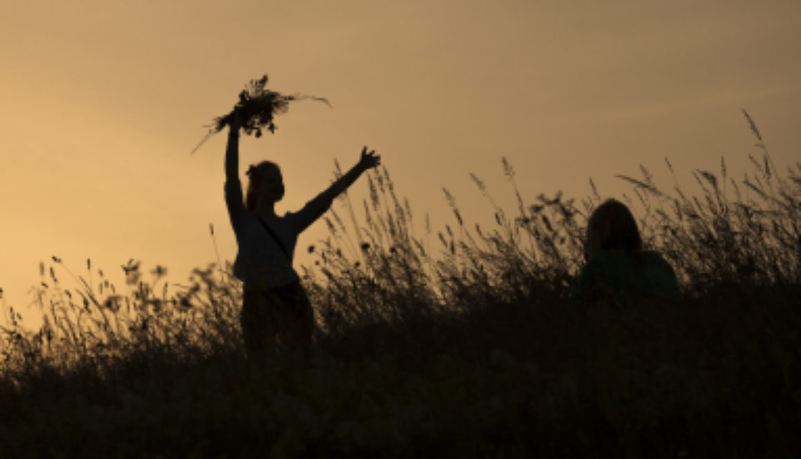 Silhouettes of happy girl picking flowers during midsummer solti
